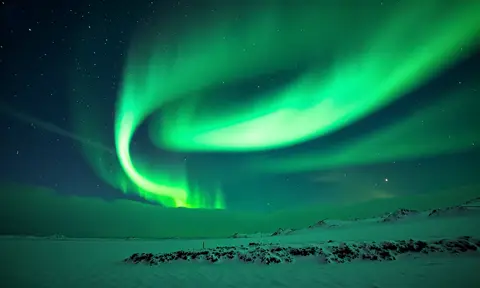 The bright green northern lights stretch across the night sky, pulsing and rippling above the snowy landscape
