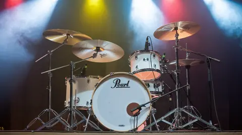 A Pearl drum set on stage, illuminated by colorful lights, ready for a live performance.