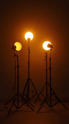 Three spotlights emitting bright orange light against a dark background, mounted on tripod stands.